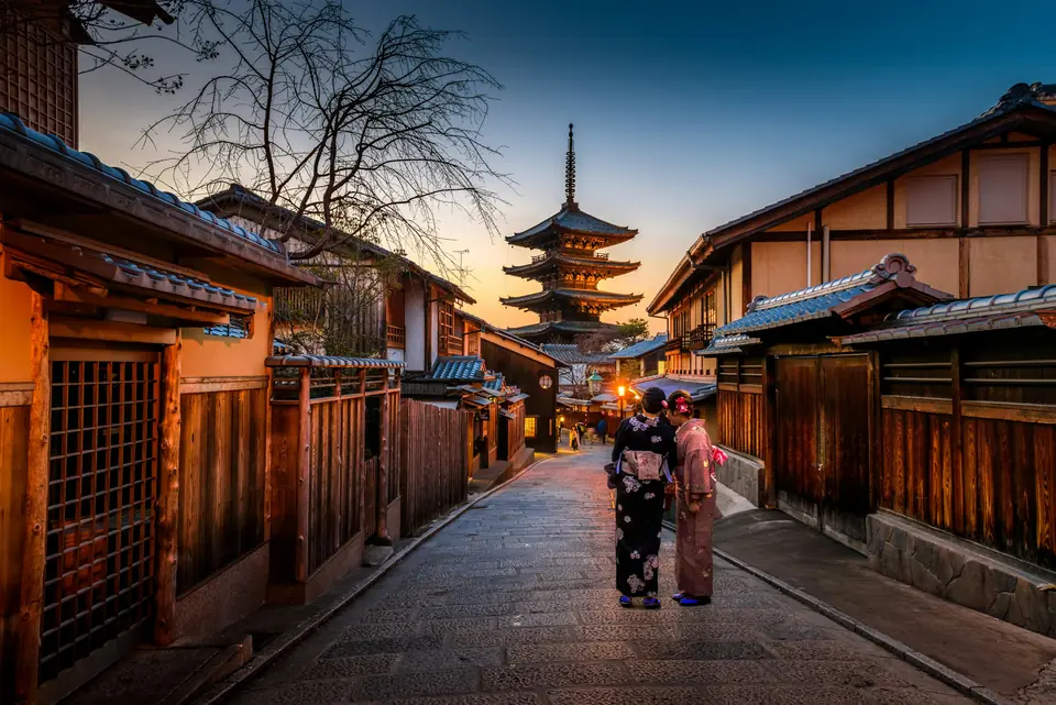 Two people in kimono walking up a quiet Kyoto lane toward the Yasaka Pagoda at dusk