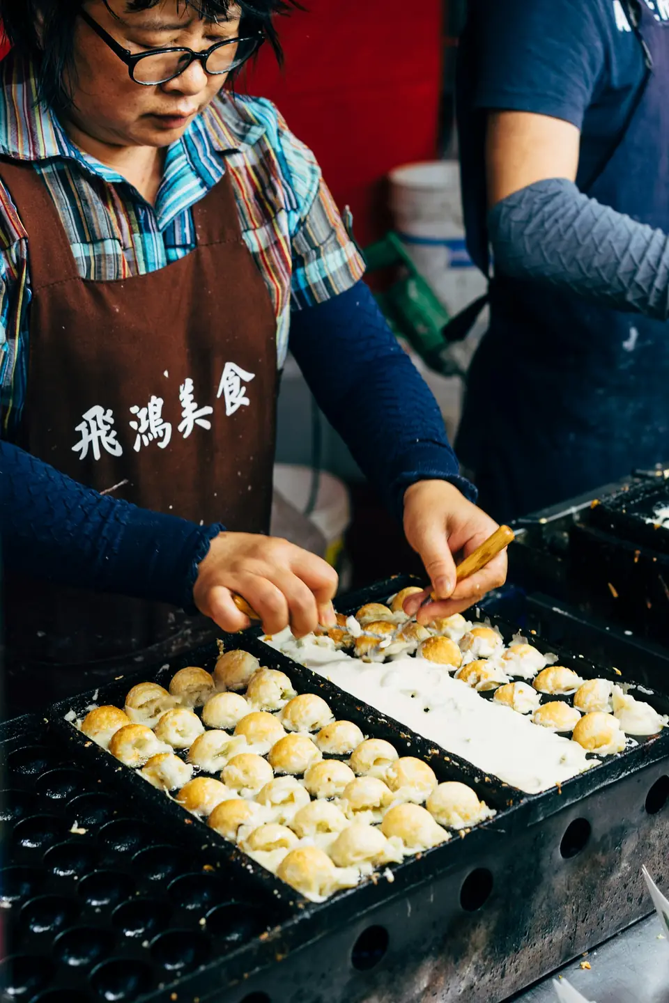 A vendor turning takoyaki at a street stall