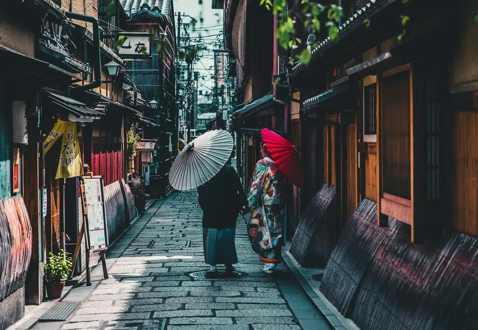 Two people with paper umbrellas walking a wet stone lane in Kyoto